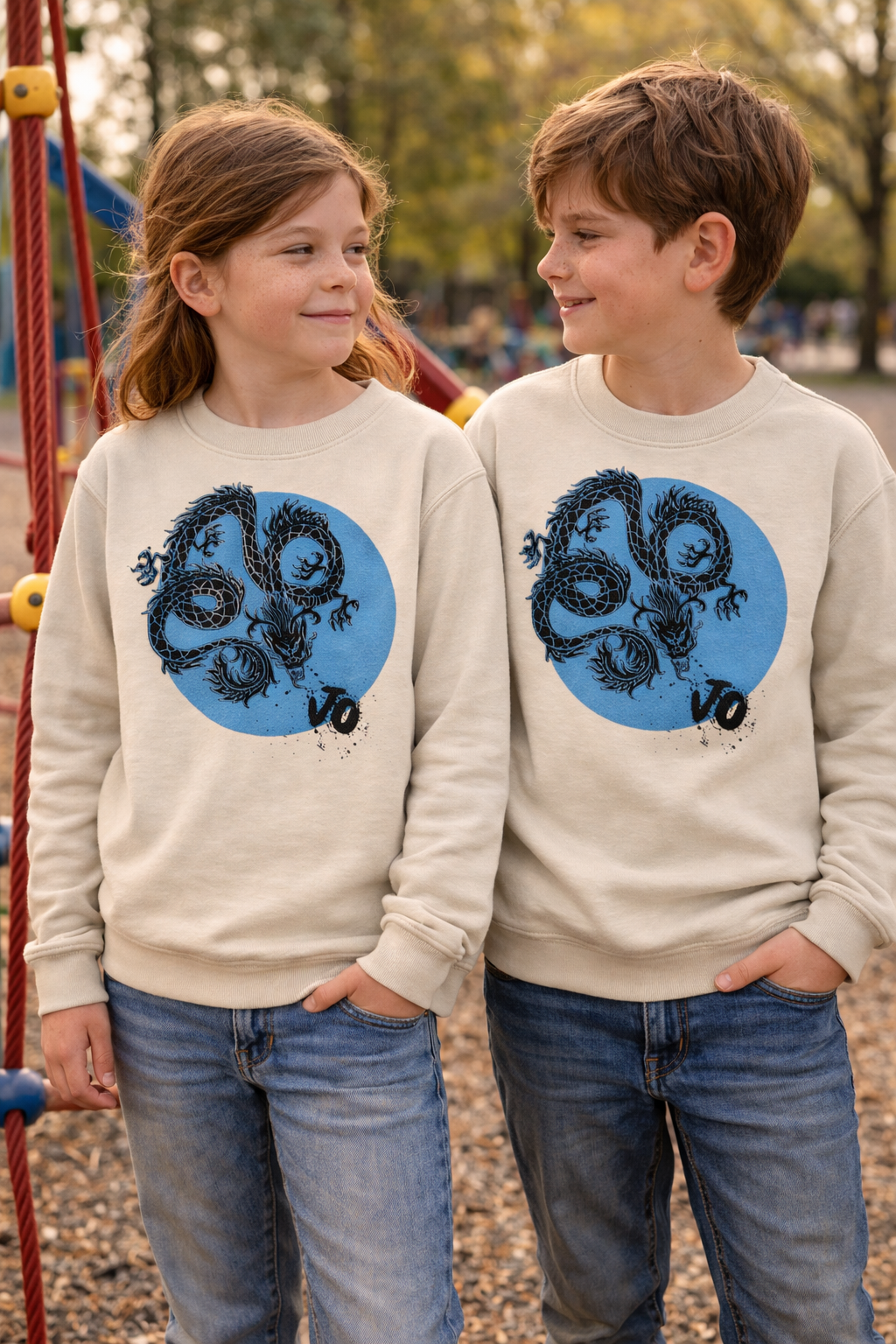 Two children wearing matching beige sweatshirts with blue circles and black designs on a playground.